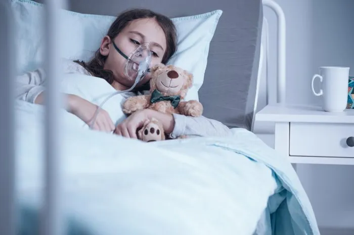 kid with cystic fibrosis lying in hospital bed with oxygen mask and plush toy