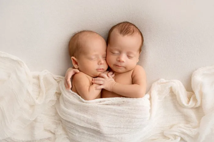 tiny newborn twins boys in white cocoons on a white background a newborn twin sleeps next to his brother newborn two twins boys hugging each other professional studio photography