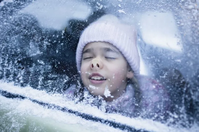 little girl wearing in winter clothes pressed her face against car window glass funny flattening nose, family road trip in winter, active weekend