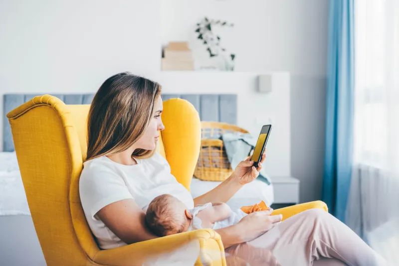 mother using digital tablet while carrying her baby at home