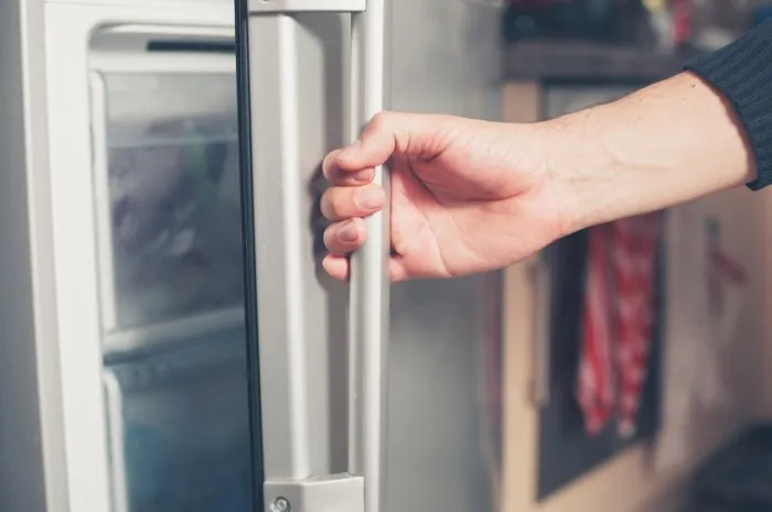 the hand of a young man is opening a freezer door