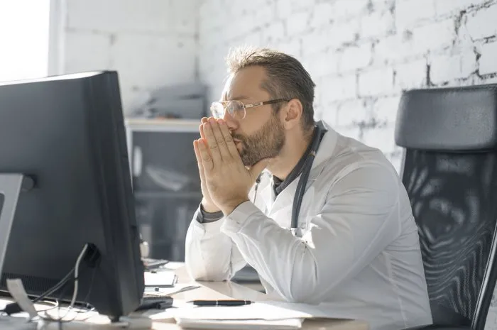 the doctor sits in the office in front of the monitor he looks thoughtfully and sadly at the monitor bad news