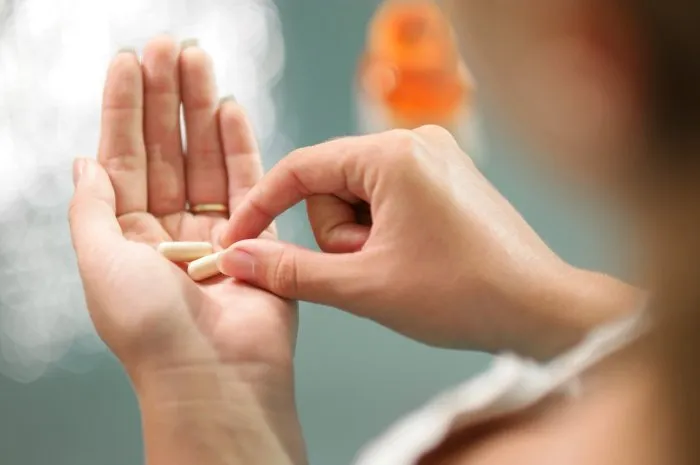 close up view of young woman holding ginseng vitamins and minerals pills in hand with capsule bottle on table high angle view