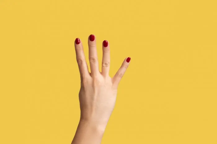 profile side view closeup of woman hand with red manicure showing number four 4 with hand indoor studio shot isolated on yellow background