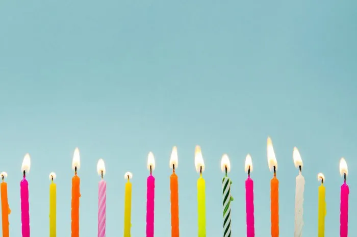 set of many different color shape and pattern birthday candles burning isolated on blue happy birthday card design concept bottom lower border edge a lot of copy space