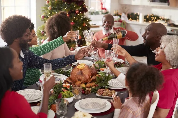 multi generation mixed race family pouring champagne and raising glasses to make a toast sitting at the christmas dinner table, elevated view