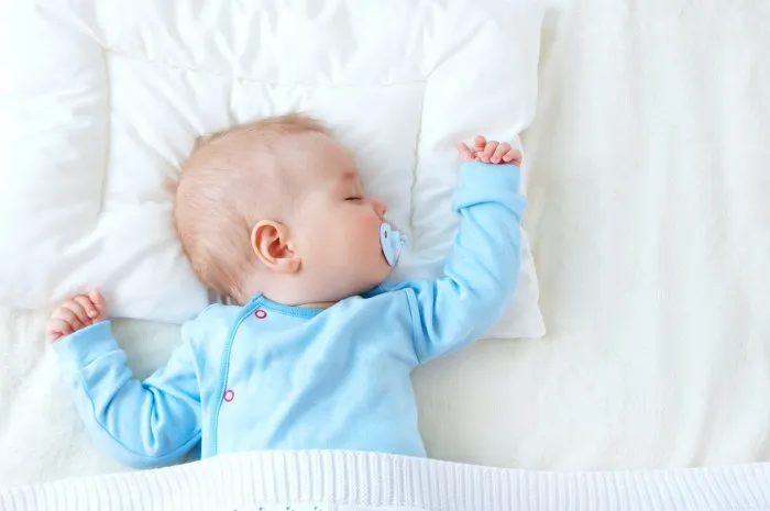seven month old baby sleeping on white blanket and pillow sleepy child on soft bedding with pacifier