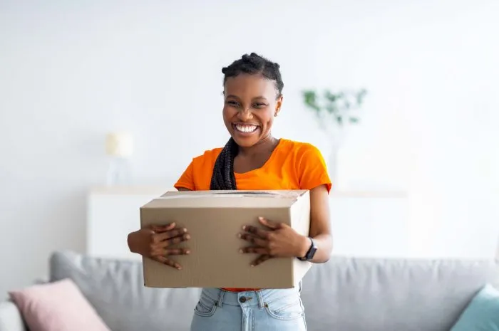 overjoyed black lady holding cardboard parcel, receiving desired delivery, getting her online order at home excited african american woman satisfied with her internet purchase