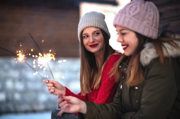 photo of smiling young women holding sparkling sticks in the winter