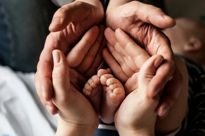 young family of mother of the father and kid mother and the father hold legs of the newborn child in the palms