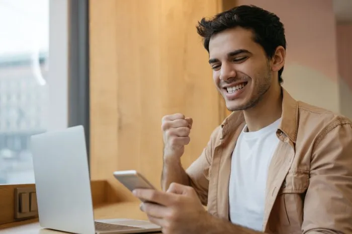 young handsome indian man holding mobile phone, communication, receive text message, reading good news asian business man with happy emotional face celebration success, sitting in modern office