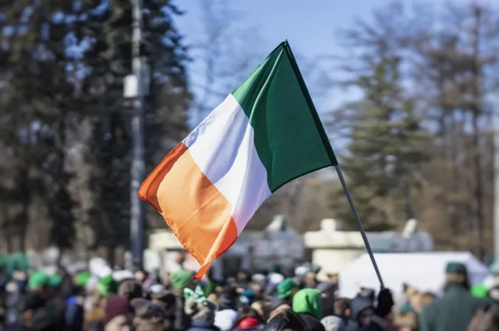 flag of ireland close-up in hands on background of blue sky during the celebration of st patrick's day in the city