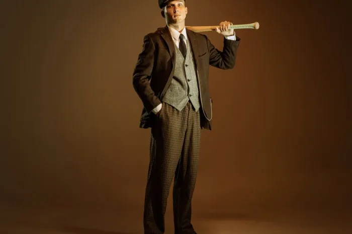 retro style portrait of young man in image of english gangster, businessman wearing suit and cap standing isolated over dark vintage background concept of business, personality, emotions, fashion