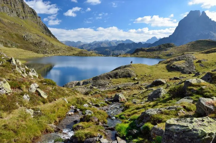 a mountain stream runs to the alpine lake gentau there are tourists and the recognizable summit pic du midi d'ossau in the background