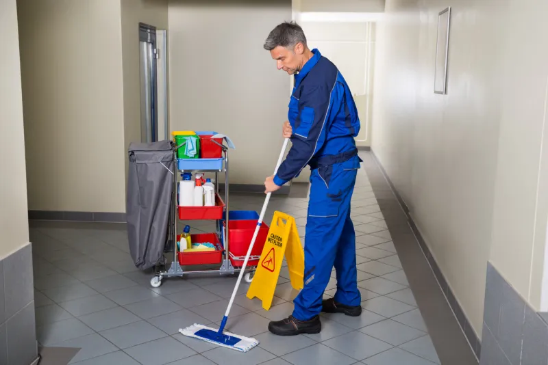 full length of mature male worker with broom cleaning corridor