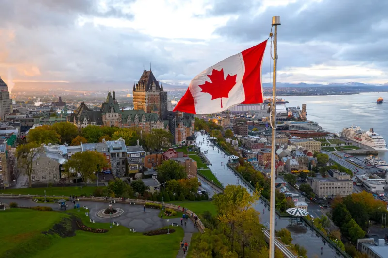 a flowing canadian flag on a flagpole taken at sunset with old quebec city and the st lawrence river in the background aerial hdr view