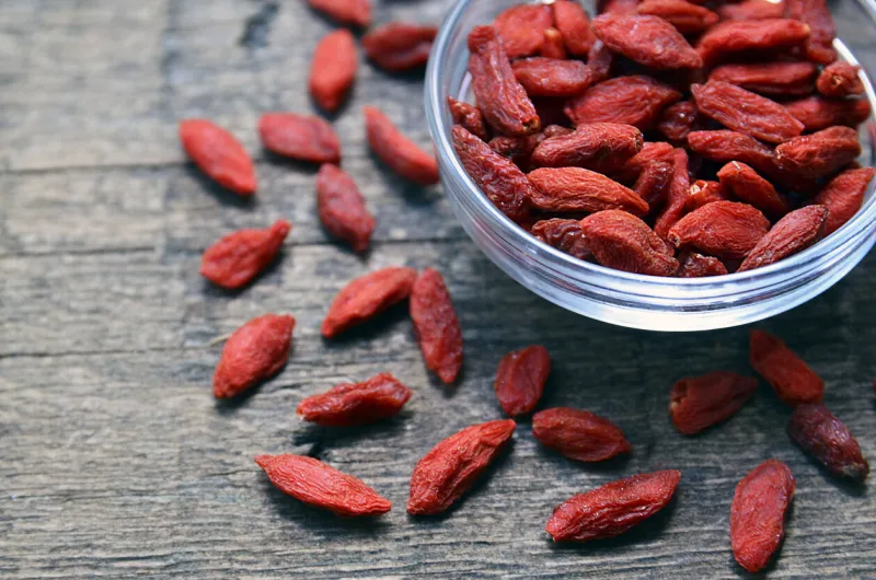 red dried goji berries in a glass bowl on old wooden backgroundselective focushealthy food or diet concept