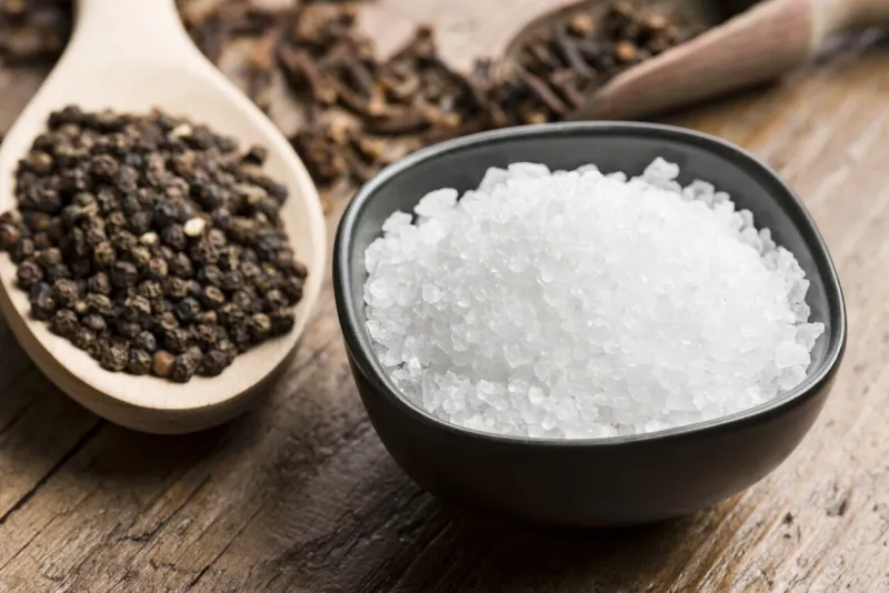 natural salt into black bowl with peppercorn and cloves on wooden table