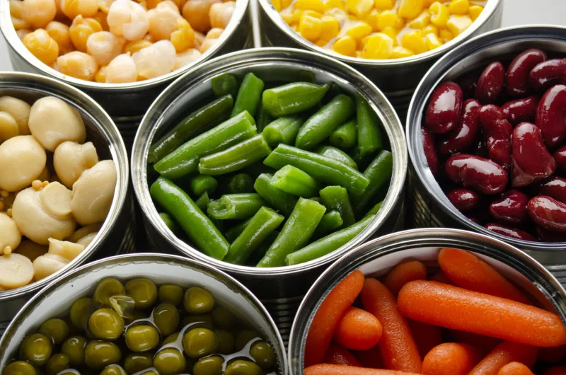 canned vegetables in opened tin cans on kitchen table non-perishable long shelf life foods background
