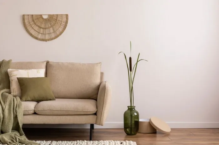 minimalist composition of elegant and outstanding space with beige sofa, boucle rug, vase, green plaid, decoration and elegant personal accessories beige wall home decor template