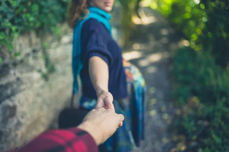 a young pregnant woman is leading her boyfriend by the hand