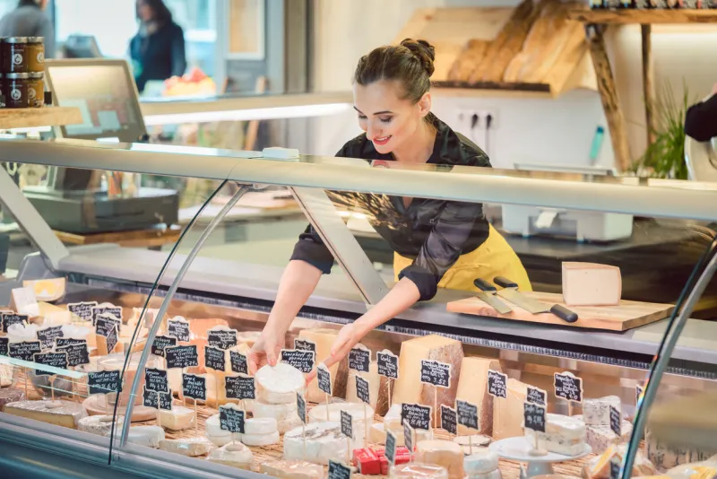 shop clerk woman sorting cheese in the supermarket display to sell it