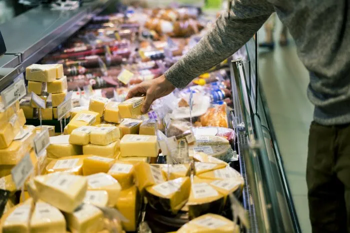 close up person choosing piece of cheese in food shop