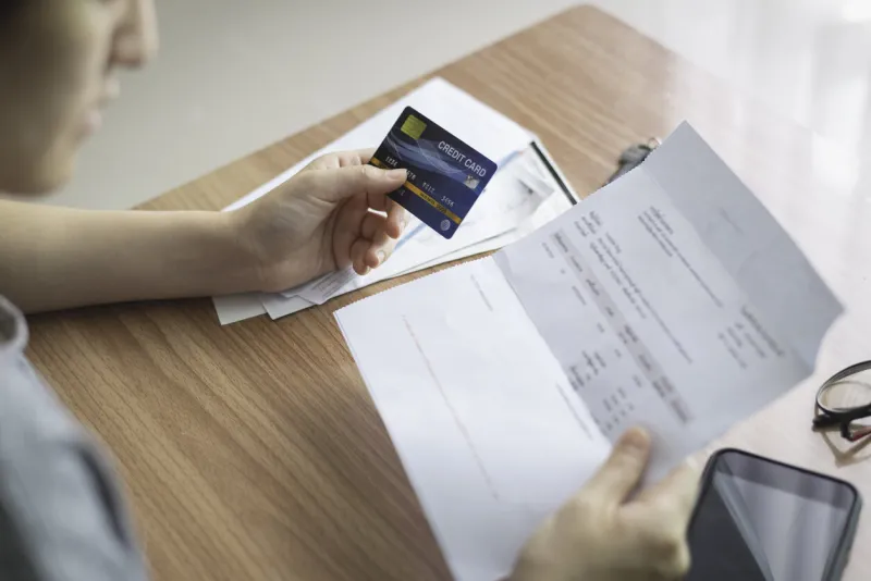 top view of women hand hold credit card and checking, verify, validate, analysis money transaction with invoice, bills and in the frame include smartphone and glasses