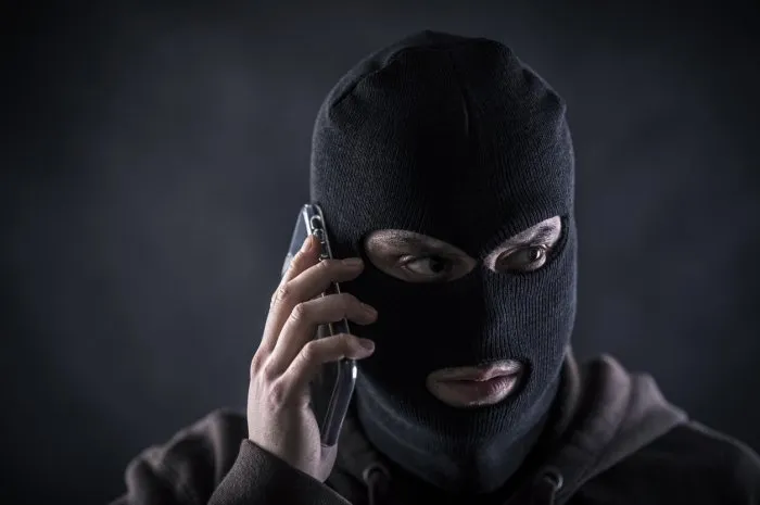 criminal wearing black balaclava and hoodie with a smartphone in the dark
