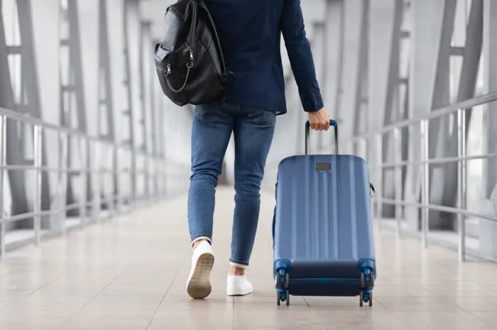unrecognizable man with bag and suitcase walking in airport terminal, rear view of young male on his way to flight boarding gate, ready for business travel or vacation journey, cropped, copy space