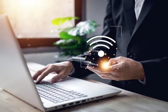 businessman hand using smartphone with wifi symbol and hands typing notebook (laptop) business technology link digital concept