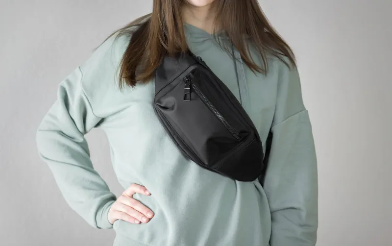 girl in a hoodie with a bag on her chest close up isolated on a gray background