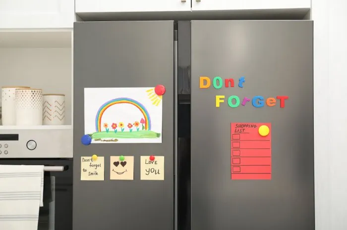 modern refrigerator with child's drawing, notes and magnets in kitchen