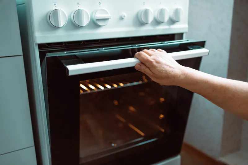woman hand opening oven door in kitchen at home door is open and light is on, home cooking