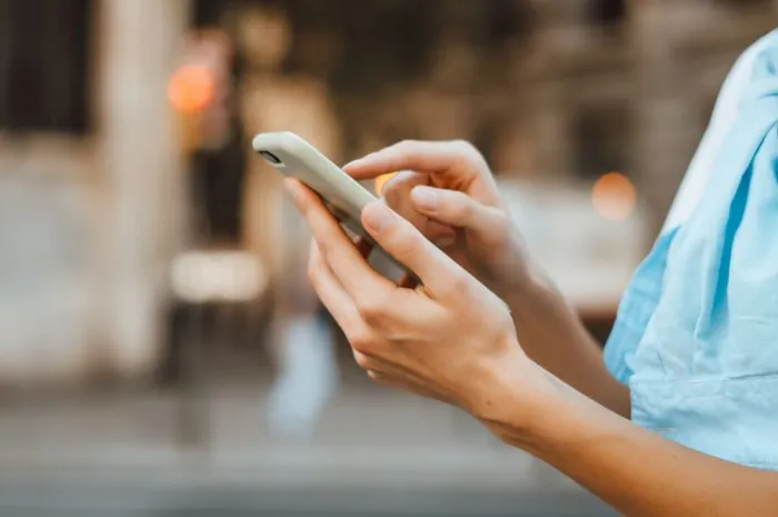 close-up photo of female hands with smartphone young woman typing on a mobile phone on a sunny street