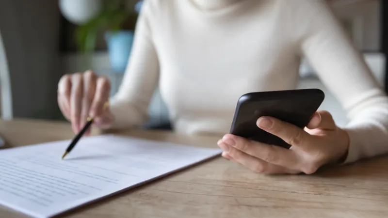 close up focused financier reading paper contract agreement, checking latest investment news in smartphone application indoors, concentrated female editor reading document or report at workplace