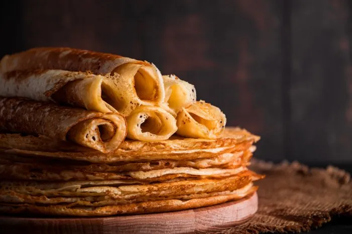 traditional russian food - thin pancakes a stack of crepes on a dark brown wooden background rustic style, place for text