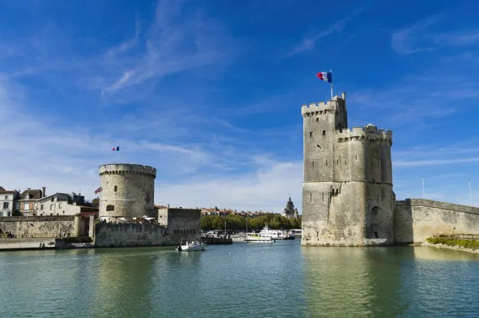 view of the entrance to the old port of the french city of la rochelle with the two medieval towers and blue sky with light clouds