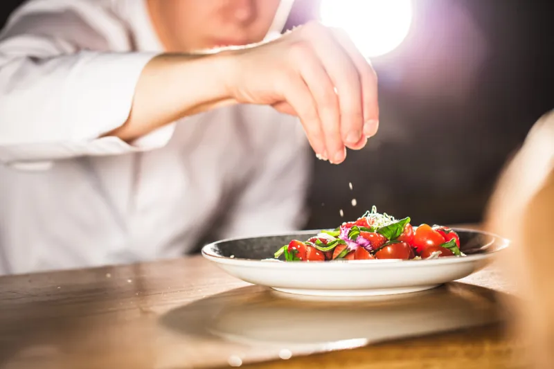 closeup mid section of a chef putting salt in the kitchen