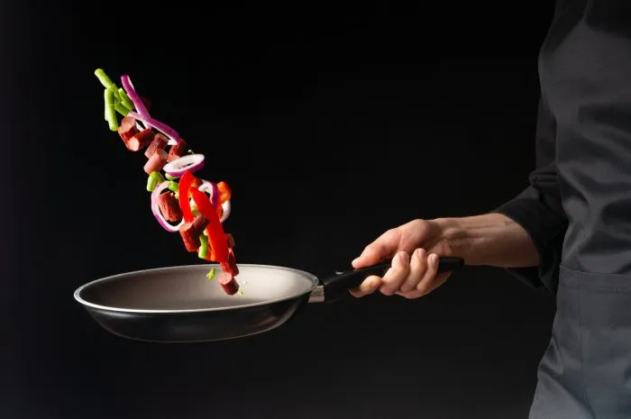 chef preparing pepperoni sausages with green beans, sweet bell peppers and red onion rings, on a black background, close-up