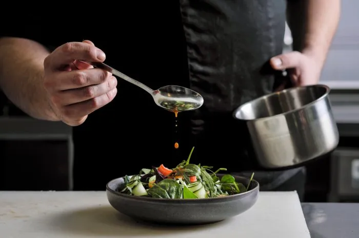 close-up of the hands of a male chef on a black background pour sauce from the spoon on the salad dish food decoration