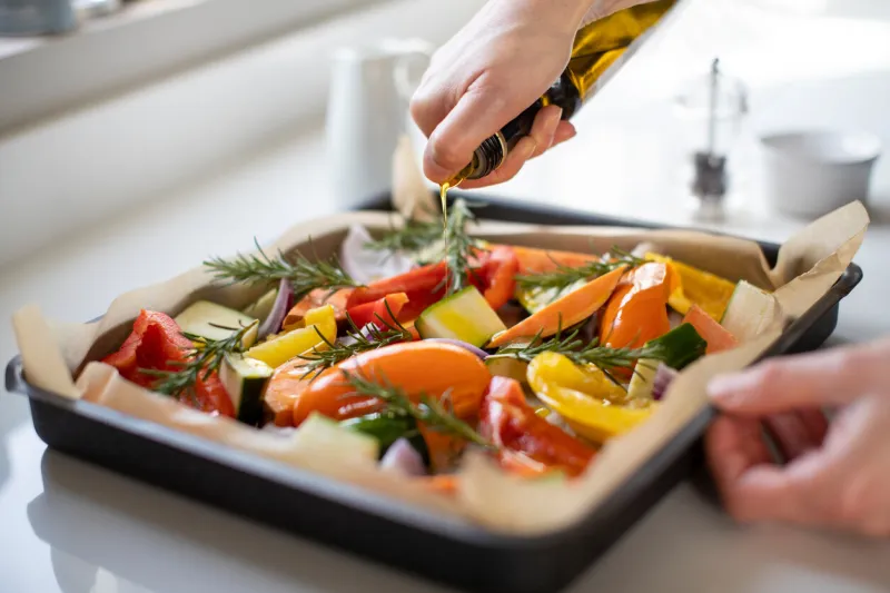 close up of seasoning tray of vegetables for roasting with olive oil ready for vegan meal
