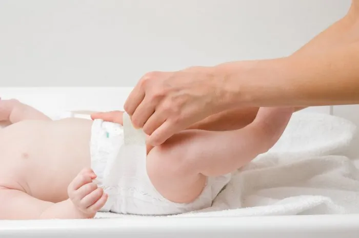 young mother hands changing diaper for baby on white towel closeup