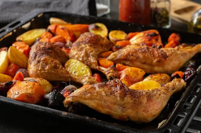 homemade oven roasted chicken legs with colorful vegetables on a baking tray - ready to eat