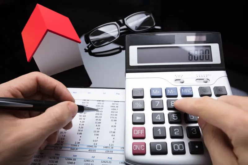 close-up of a businessperson's hand calculating financial report with calculator