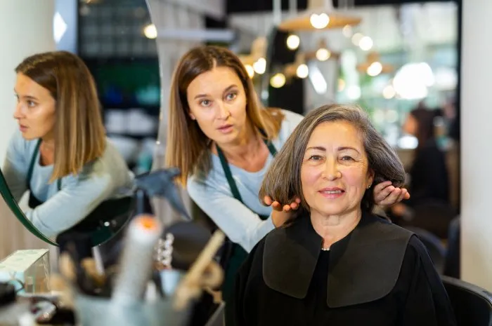 professional hair stylist discussing elderly female customer preferences in salon, choosing new hairdo