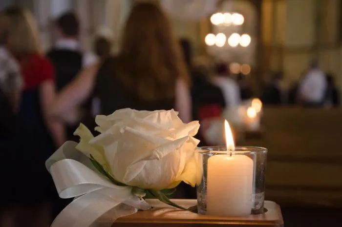 a white rose and a white candle as weddin arrangement in a church