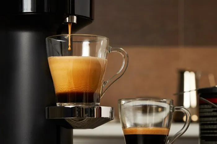 closeup of a glass cup with fresh coffee from a capsule coffee machine against the backdrop of a home kitchen selective focus