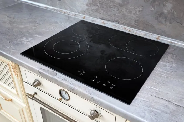 modern kitchen interior with black induction or electric hob stove cooker with ceramic top surface with marble countertop and wall decorated with stone