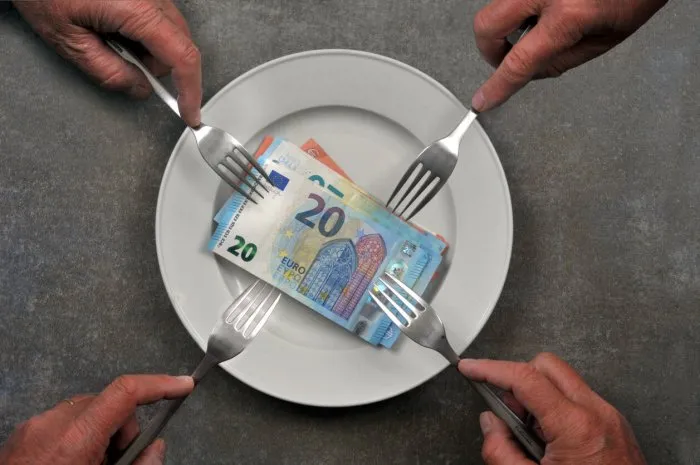 plate with banknotes and several hands with forks